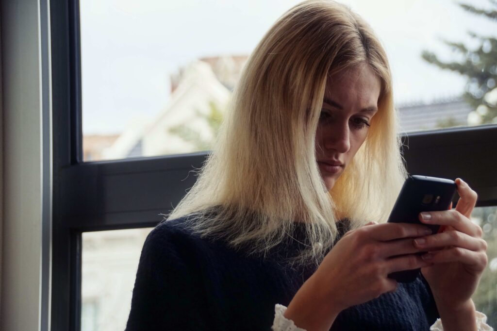 Femme assise seule regardant son téléphone avec expression mélancolique, symbolisant l'attente du retour d'un ex-partenaire borderline