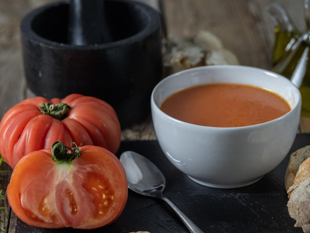 Gros plan sur une soupe de légumes avec une tomate fraîche à côté, illustrant quel légume fait tourner la soupe et comment l'éviter.