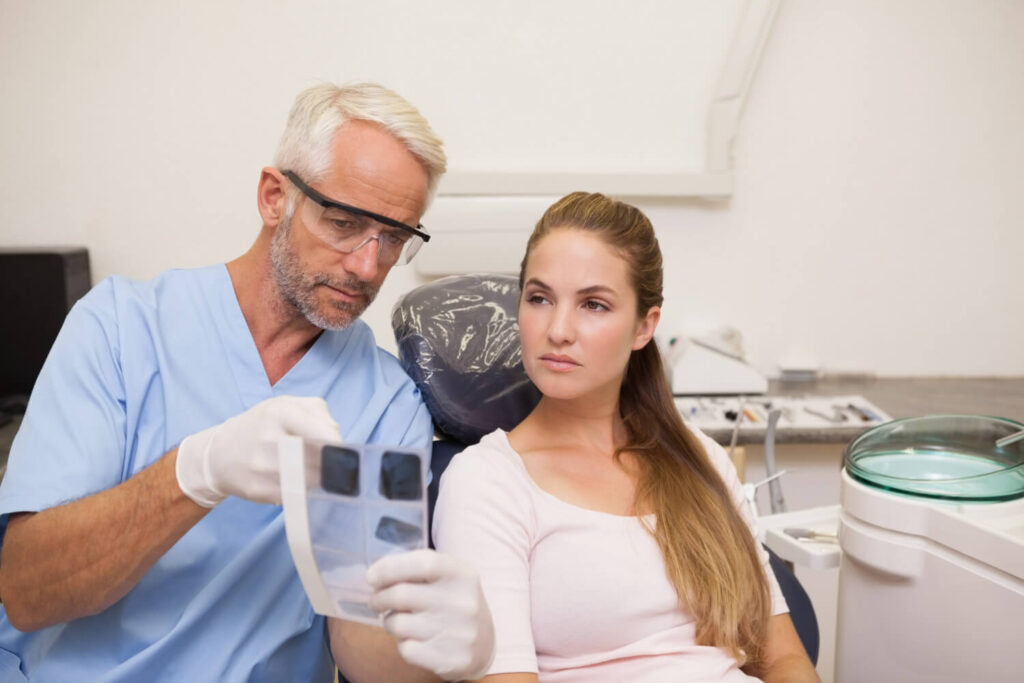 Dentiste discutant d'un échec d'implant dentaire sur une radio avec un patient pour trouver une solution de remboursement