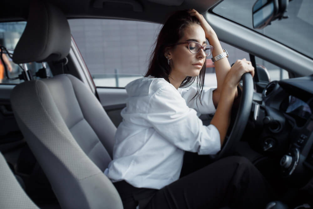 Peut-on conduire juste après une séance de kiné vestibulaire ? 4 Personne assise sur le siège conducteur d'une voiture, se tenant la tête, l'air étourdi et désorienté.