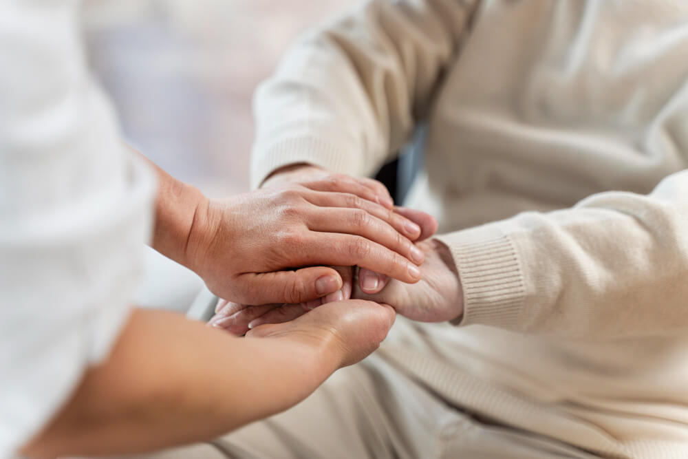 Comment meurt-on d'un cancer du côlon ? 5 Main d'un soignant tenant avec compassion la main d'un patient en fin de vie dans un lit médicalisé.