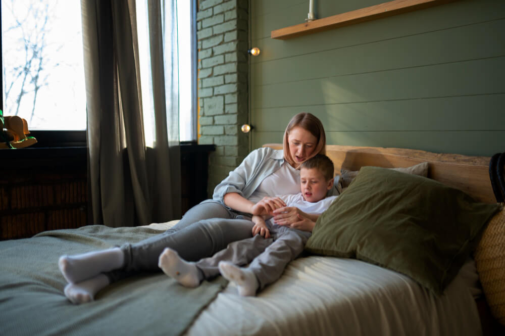 Mon enfant de 6 ans n'est toujours pas propre le jour : que faire ? 2 Parent parlant doucement et avec bienveillance à son enfant de 6 ans assis sur un lit.