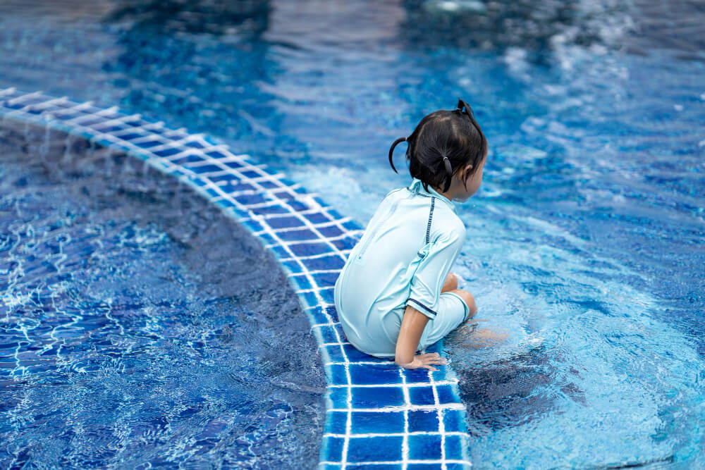 Pourquoi ma fille a-t-elle mal au ventre après la piscine ? 1 Jeune enfant se tenant le ventre au bord d'une piscine, l'air patraque.
