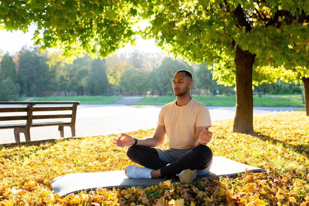 Une personne en méditation dans un parc paisible illustrant l'équilibre mental et physique.