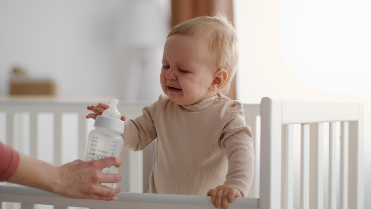 Bébé de 8 mois assis dans son lit à barreaux durant la nuit attendant son biberon.