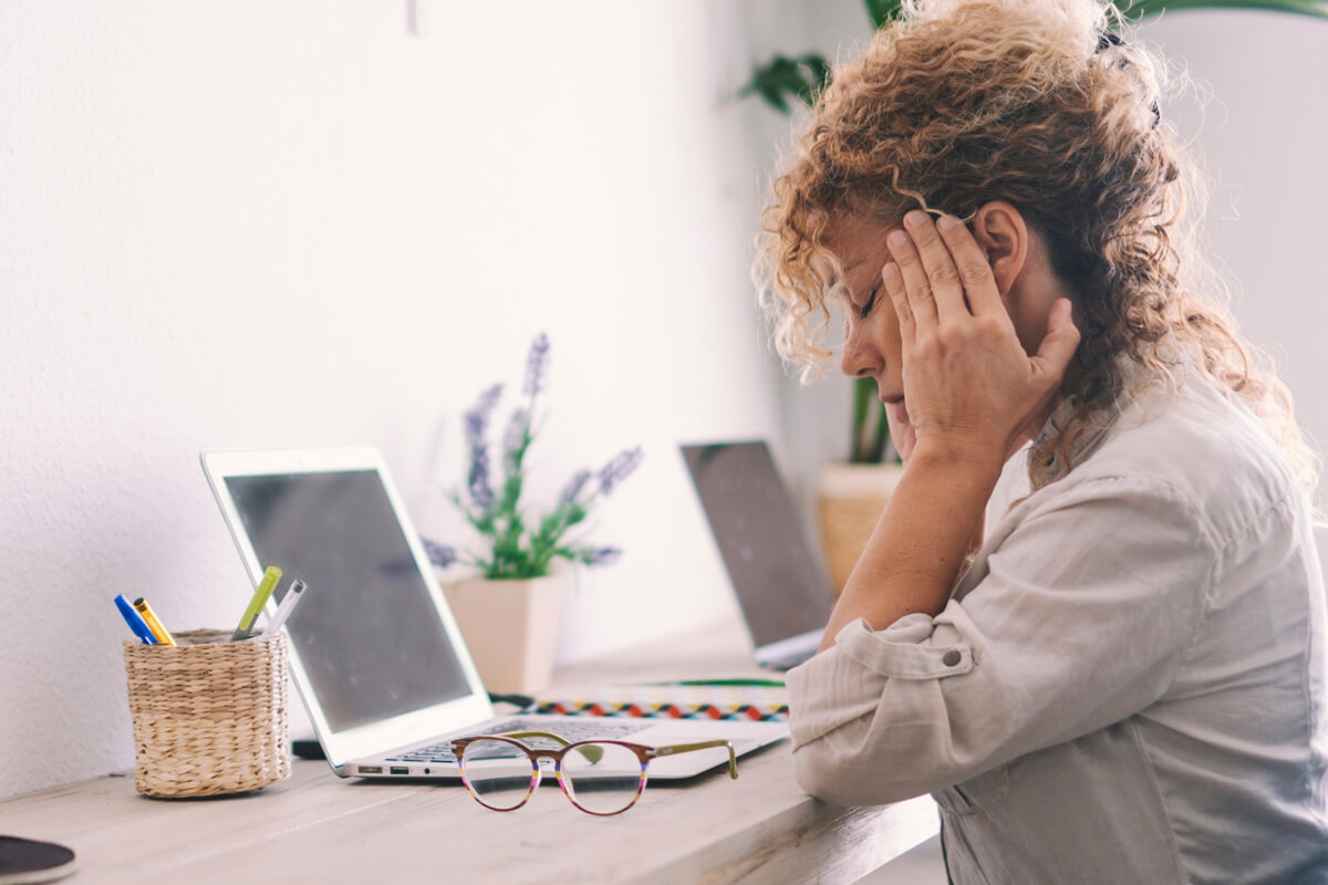 Femme au bureau se massant les tempes, frustrée de ne pas retrouver un mot précis lors d'une discussion