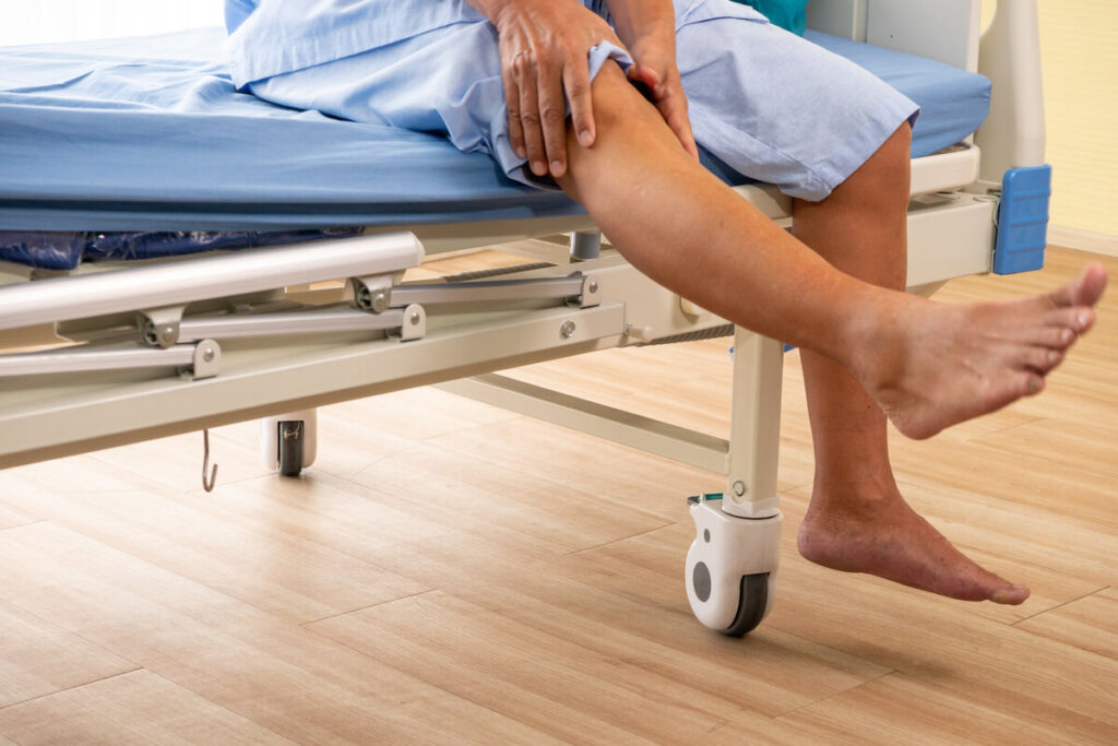 Une personne au repos sur un lit d'hôpital, touchant délicatement sa cuisse après une angioplastie de la jambe.