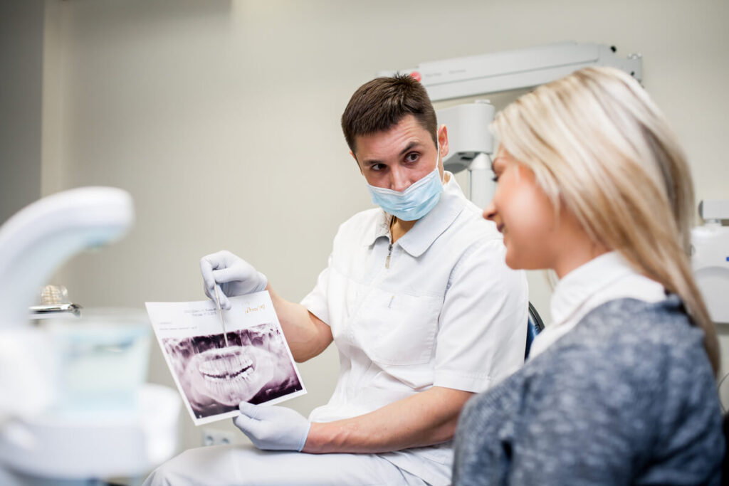 Bridge collé à ailettes métalliques : une solution idéale pour remplacer une dent ? 3 Un chirurgien-dentiste montrant une prothèse dentaire à sa patiente lors d'un rendez-vous.