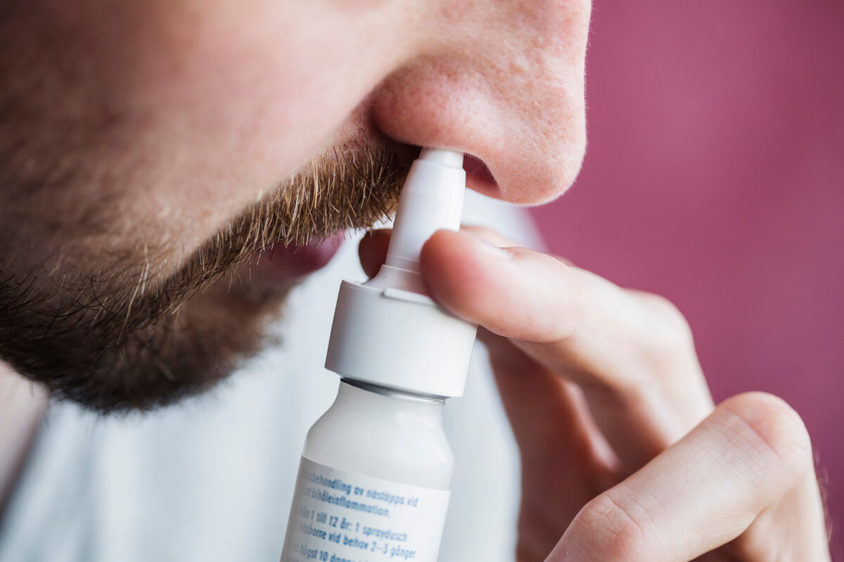 Une personne utilisant un flacon de pulvérisation nasale pour soulager une congestion liée à un rhume.