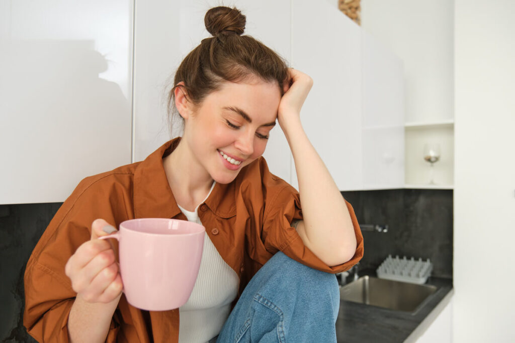 Régression du sommeil à 4 mois chez le bébé allaité : que faire ? 3 Une jeune maman souriante mais fatiguée qui se repose dans son canapé avec une tisane.