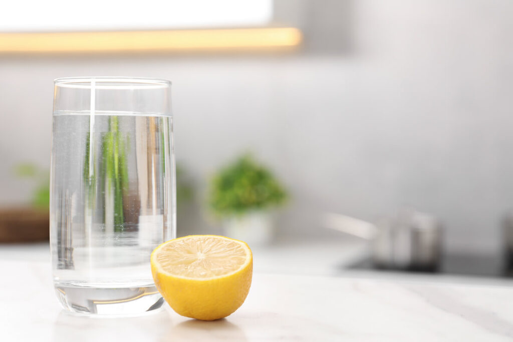 Un verre d'eau tiède avec du jus de citron frais pressé posé sur une table de cuisine lumineuse.