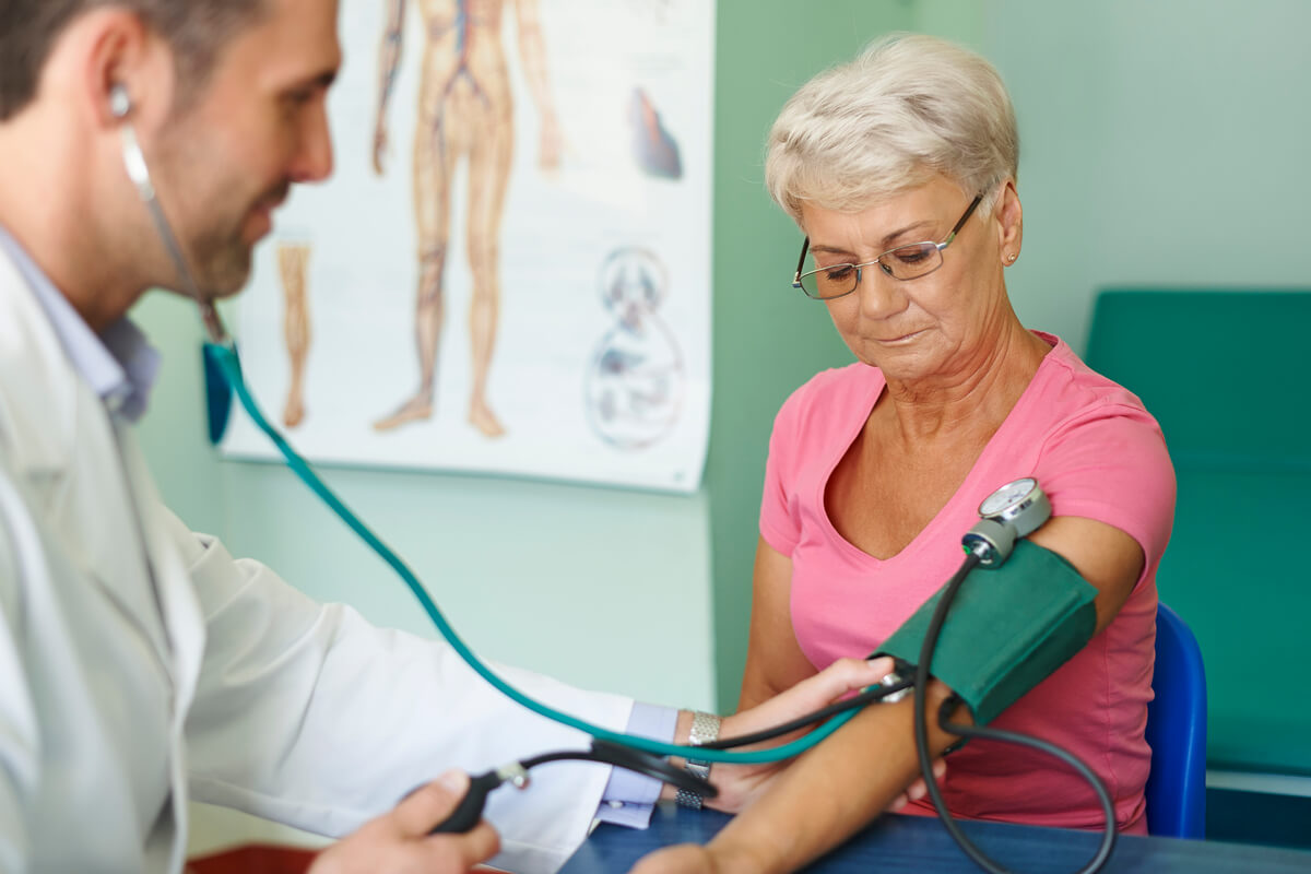 Un médecin généraliste mesurant la tension artérielle d'un patient de plus de 60 ans lors d'un bilan de contrôle.