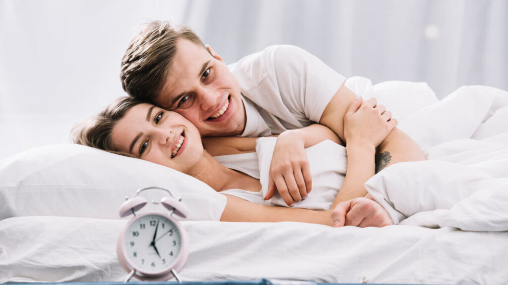 Le cododo empêche-t-il vraiment bébé de faire ses nuits ? 3 Un couple de parents qui sourit au réveil dans leur chambre à coucher lumineuse.