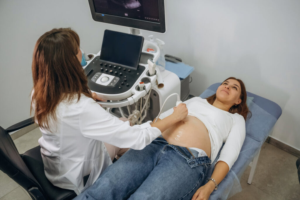 Une sage-femme réalisant une échographie de datation précoce sur le ventre d'une femme enceinte.