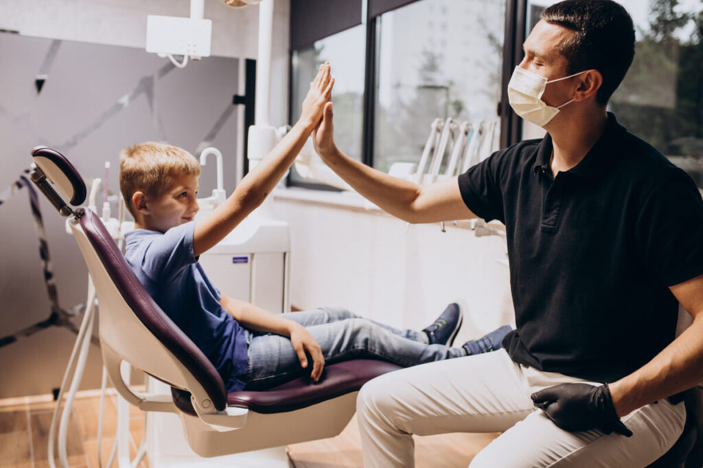 Un jeune enfant souriant assis sur le fauteuil du dentiste lors d'un contrôle dentaire ludique et sans stress.