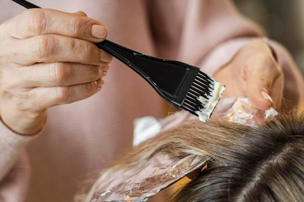 Coloration vegetale bio : choisir une formule capillaire saine et certifiee 2 Un coiffeur appliquant un soin colorant végétal et organique au pinceau sur les cheveux d'une cliente.