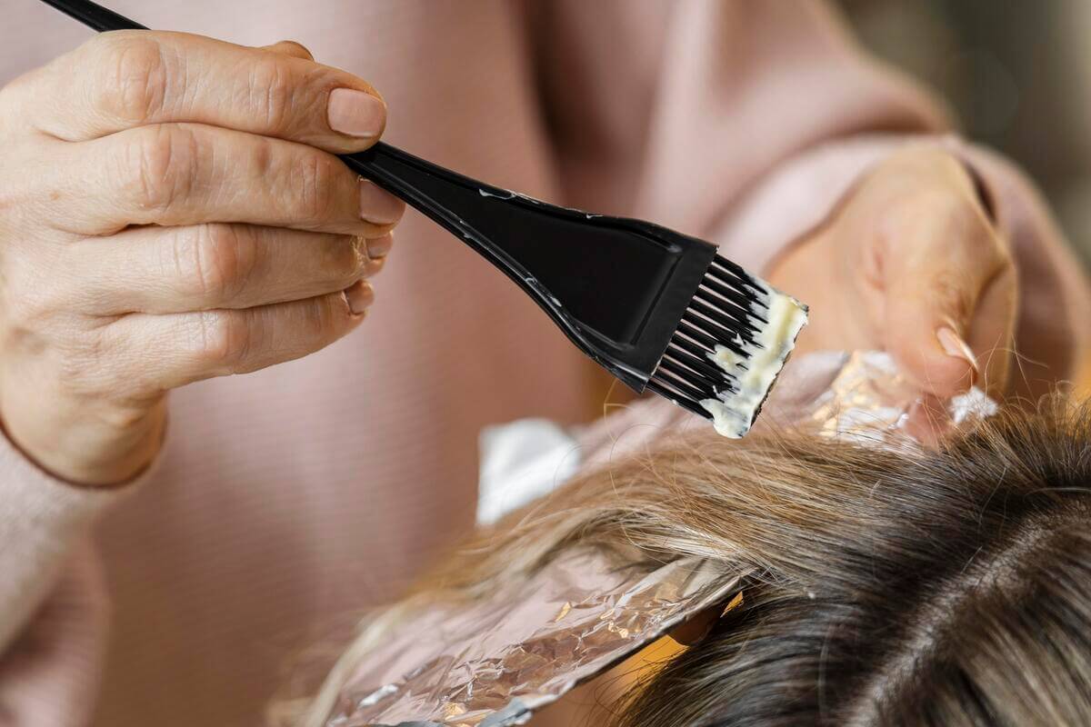 Un coiffeur appliquant un soin colorant végétal et organique au pinceau sur les cheveux d'une cliente.