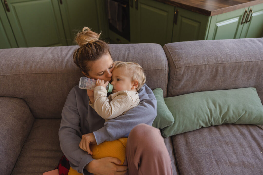 Blédine 4 mois le soir : conseils, dosage et diversification de bébé 2 Un nourrisson confortablement installé dans les bras de sa maman buvant son biberon du soir.