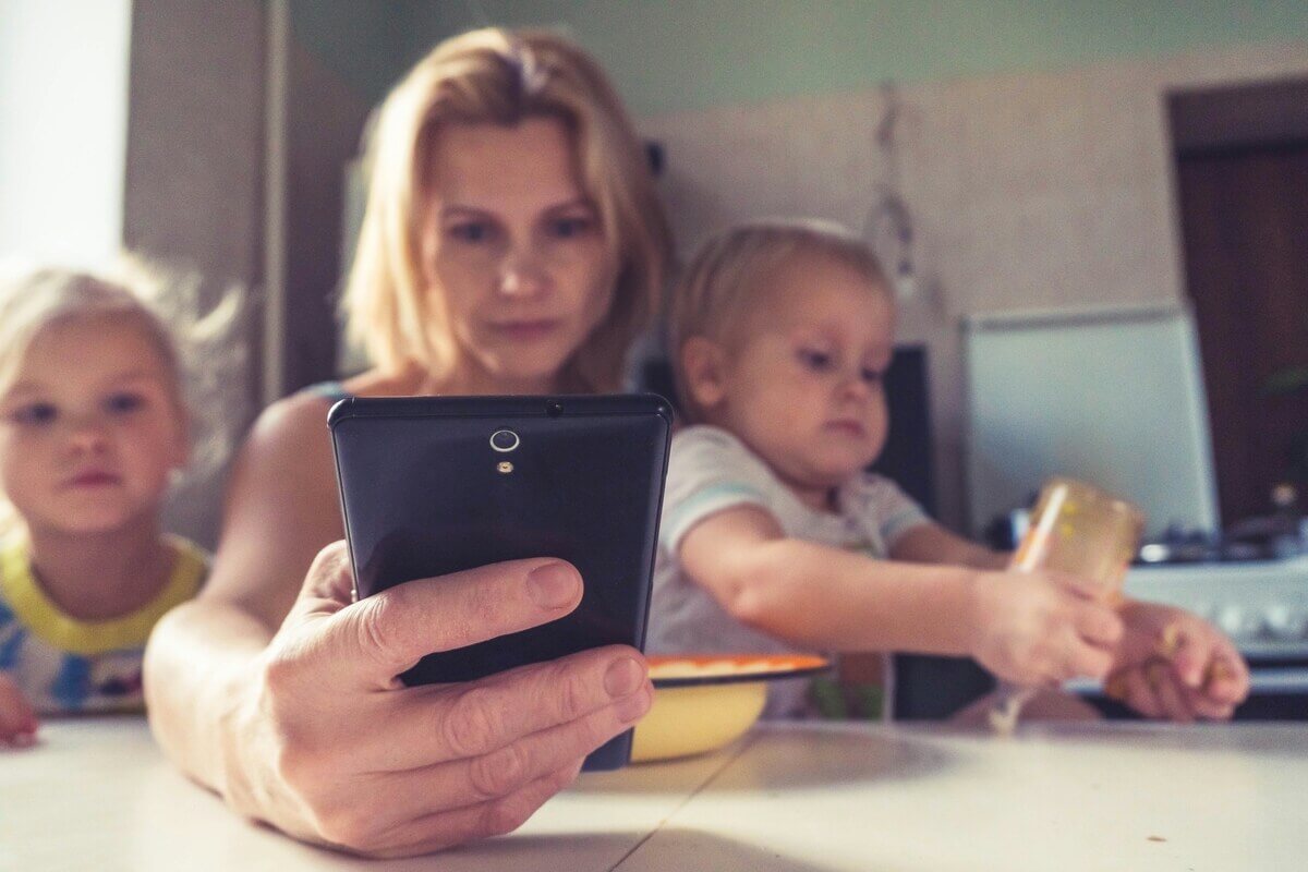 Un parent consultant une application de suivi médical sur son smartphone dans la salle d'attente d'une gare.