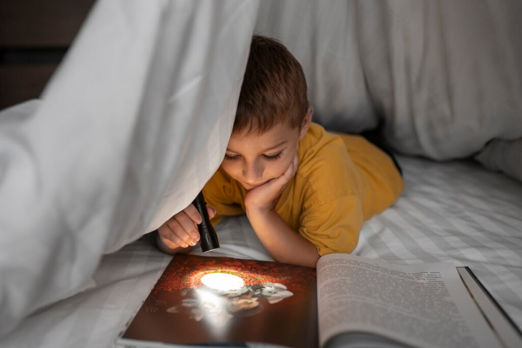 Un jeune garçon assis dans son lit regardant une ombre dans sa chambre avec inquiétude.