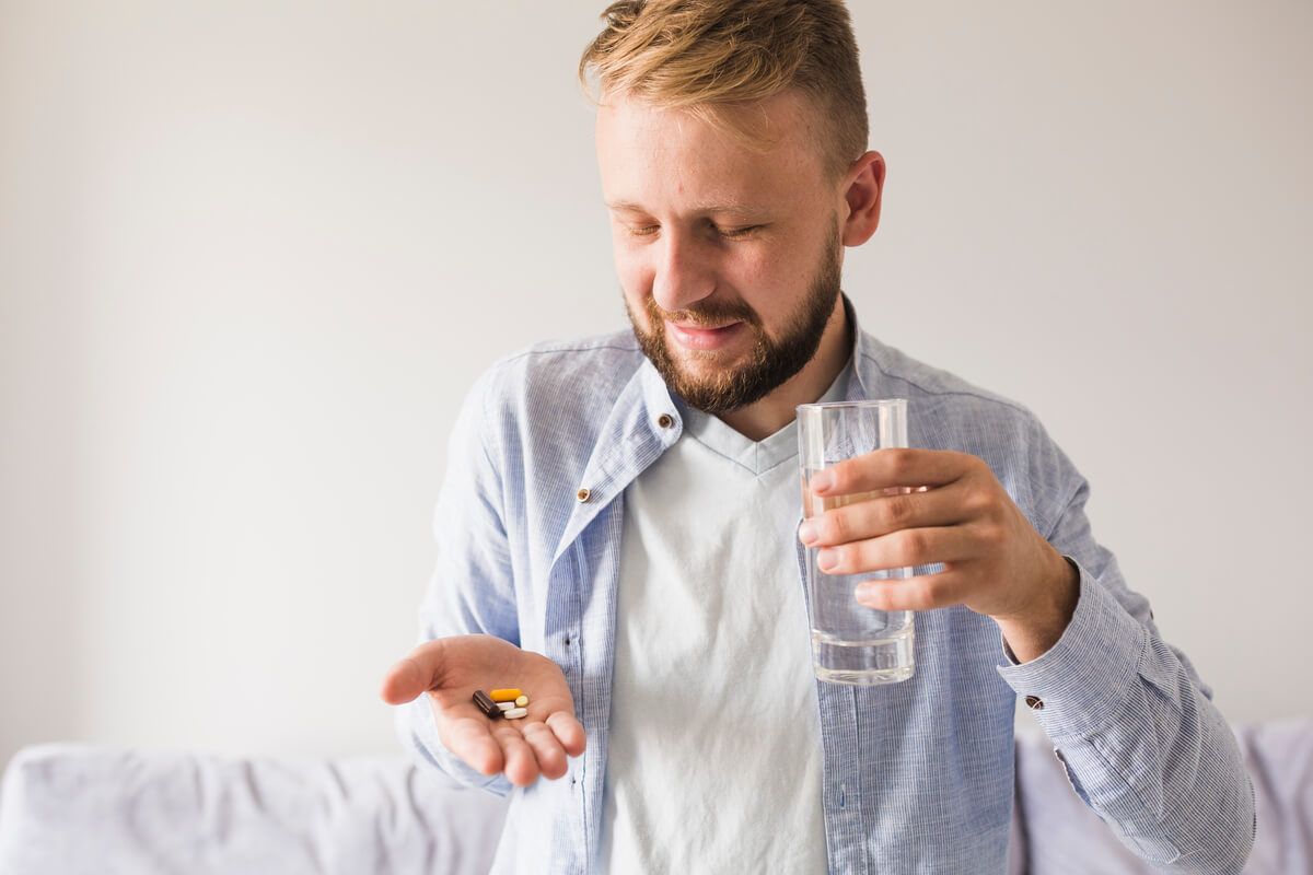 Une personne préparant ses gélules de traitement médical avec un grand verre d'eau.