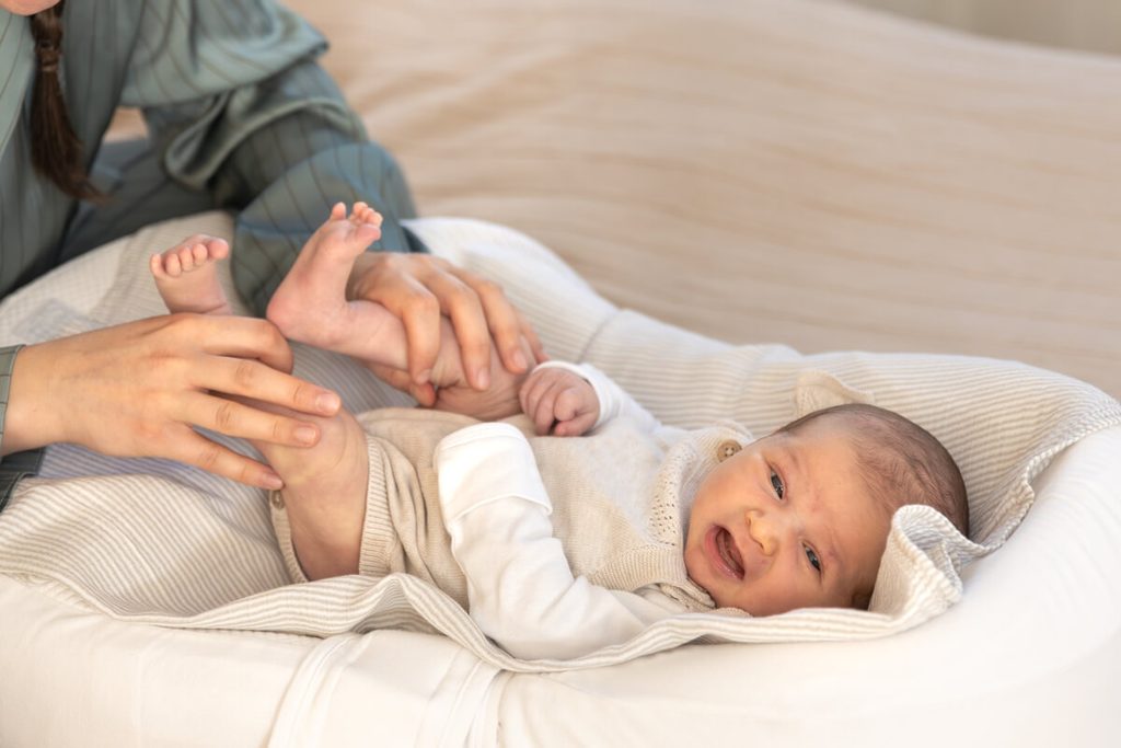 Bébé repliant ses jambes sur un ventre dur et ballonné, signe de coliques du nourrisson.