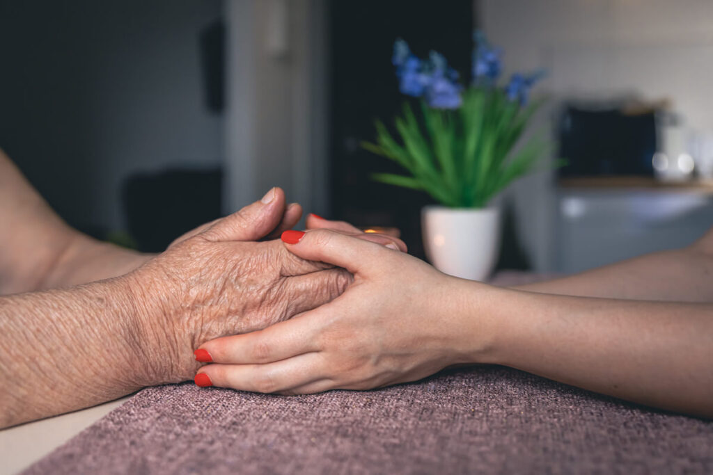 Maladie d'Alzheimer : comment reconnaître les premiers signes et réagir tôt ? 4 Un membre de la famille tenant la main d'un proche atteint de la maladie d'Alzheimer pour le rassurer.