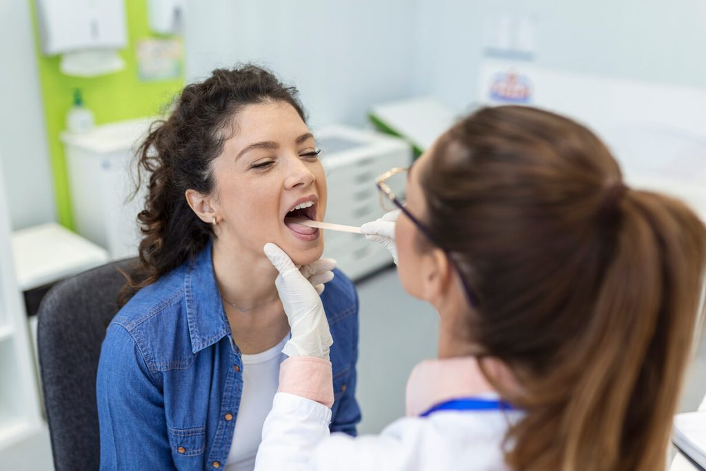 Médecin ORL réalisant un examen de la cavité buccale et de la gorge d'un patient adulte.