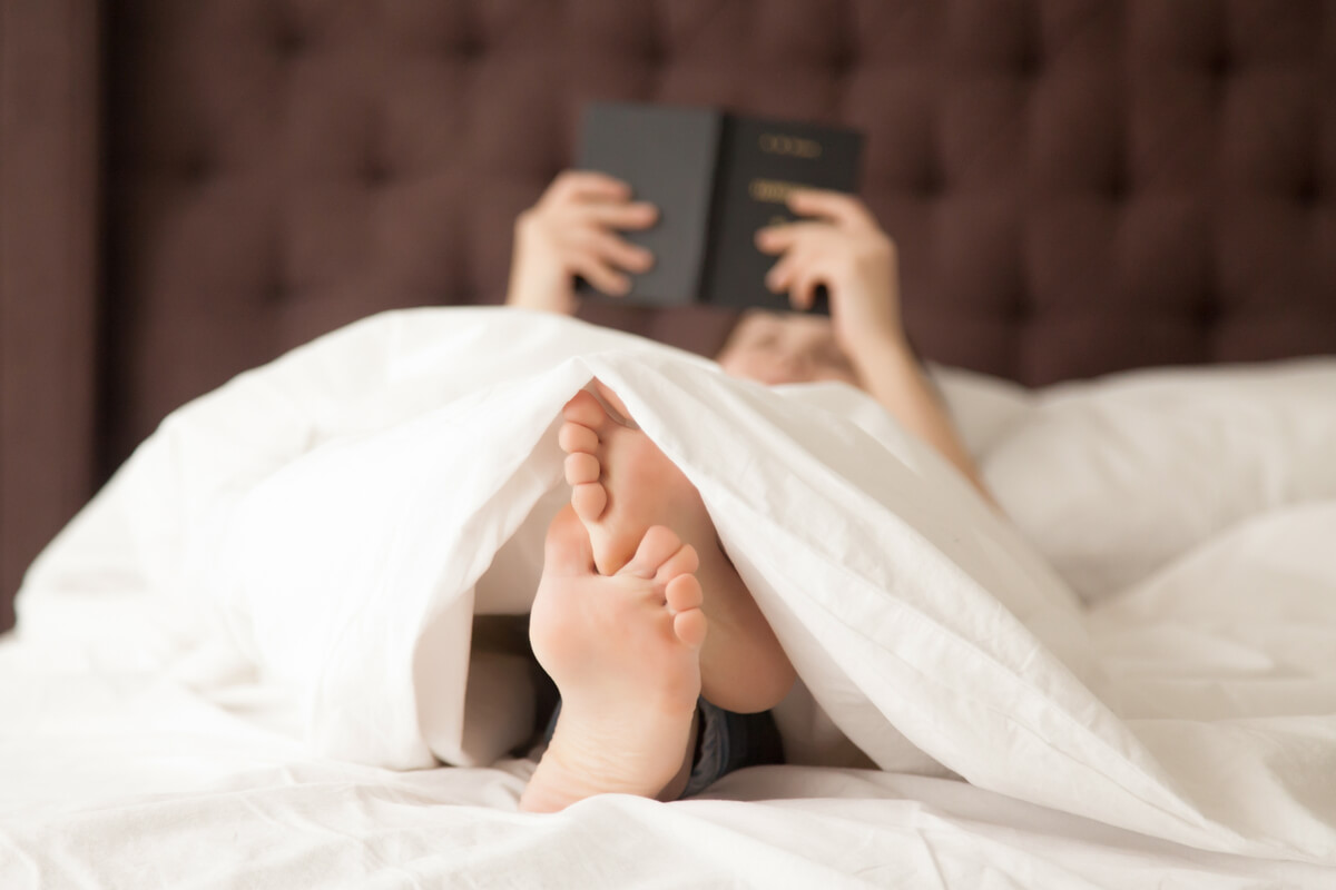 Personne assise au bord du lit massant ses pieds douloureux en pleine nuit.